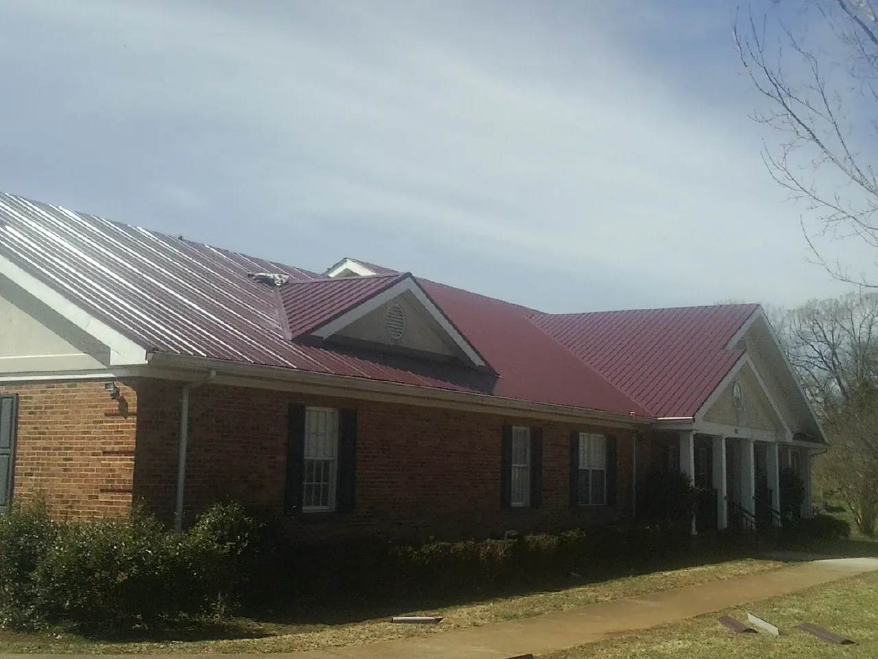 Red metal roof with gabled entries on a long brick building, from a Hail Damage Roof Repair job in Petersham