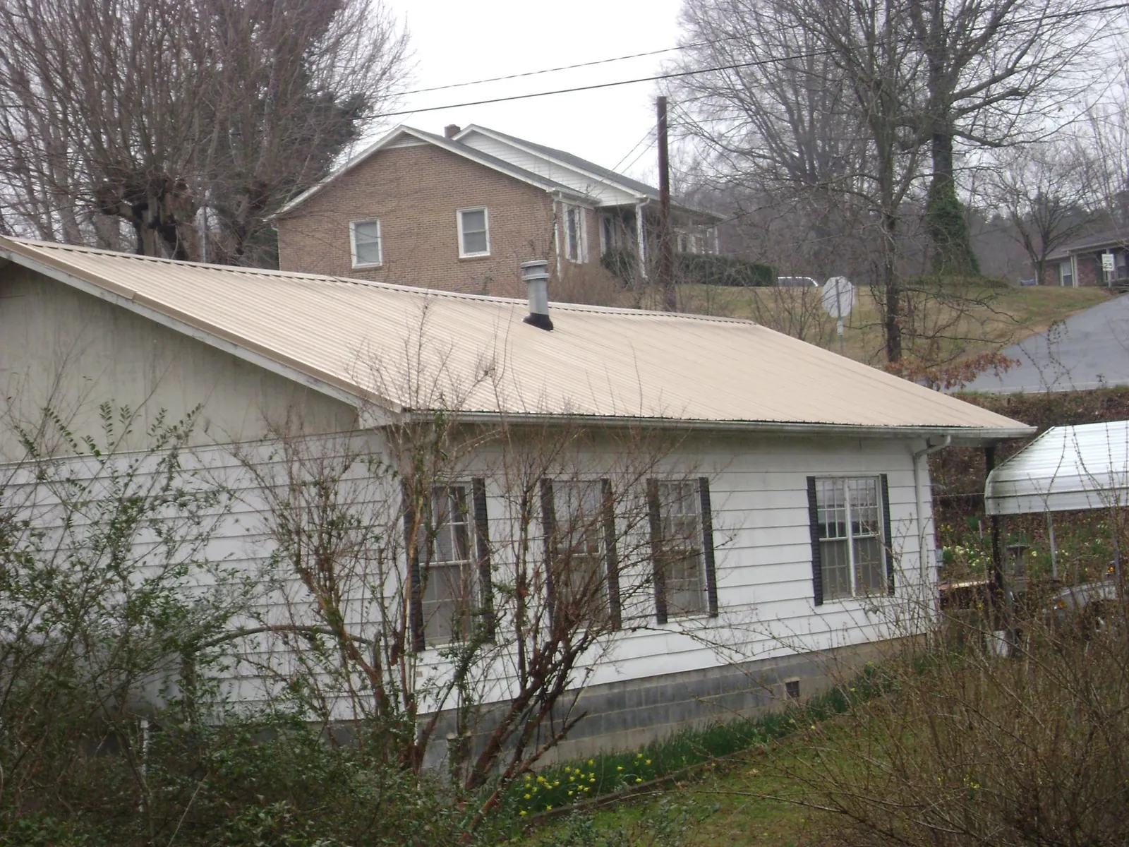 Tan metal roof on a white sided house set into a hillside — Commercial Roofing by Roofing Brothers in Petersham